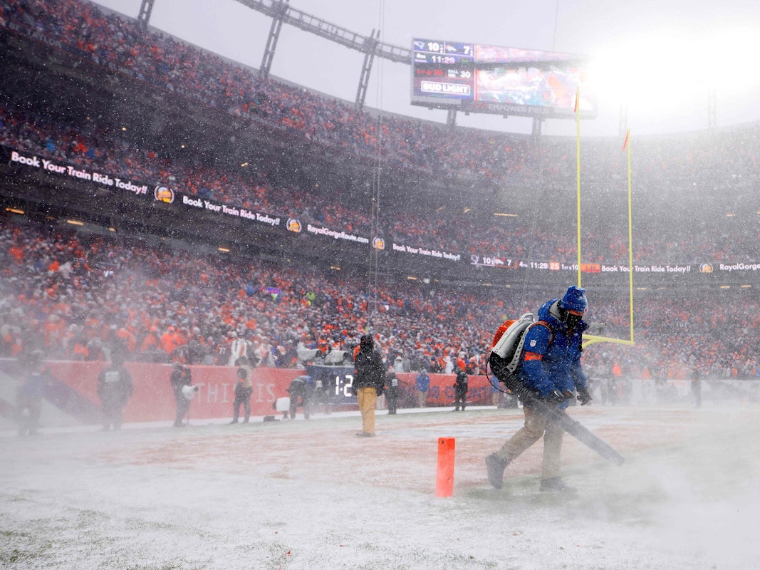 Helfer befreien das Feld im Spiel der Denver Broncos in der NFL von Schnee.
