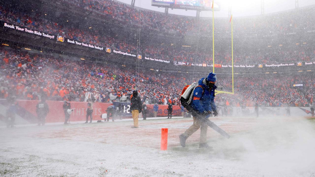 Helfer befreien das Feld im Spiel der Denver Broncos in der NFL von Schnee.