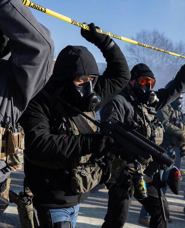 US‑Beamte gehen unter einem gelben Absperrband hindurch und tragen dabei Gasmasken.