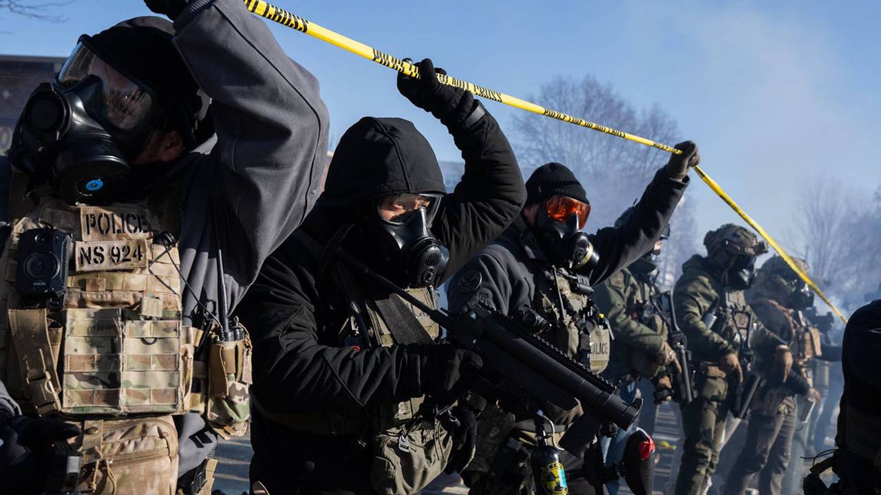 US‑Beamte gehen unter einem gelben Absperrband hindurch und tragen dabei Gasmasken.
