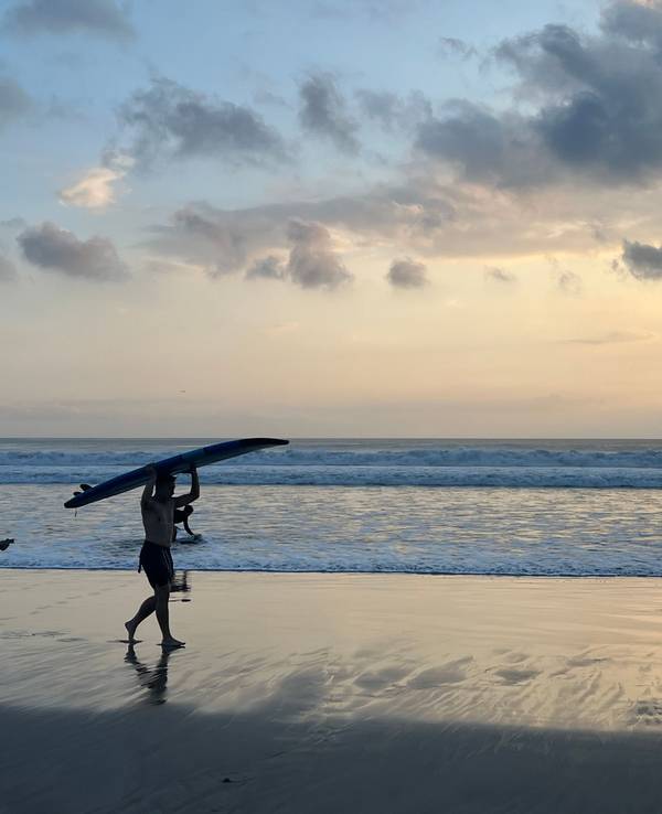 Ein Surfer läuft beim Sonnenuntergang mit seinem Surfbrett am Kuta Beach auf Bali.