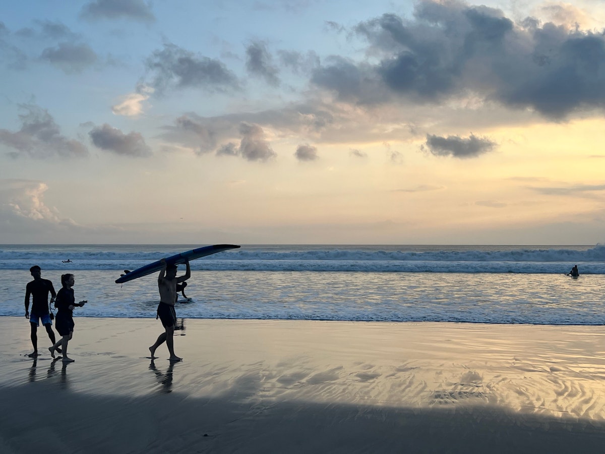 Ein Surfer läuft beim Sonnenuntergang mit seinem Surfbrett am Kuta Beach auf Bali.