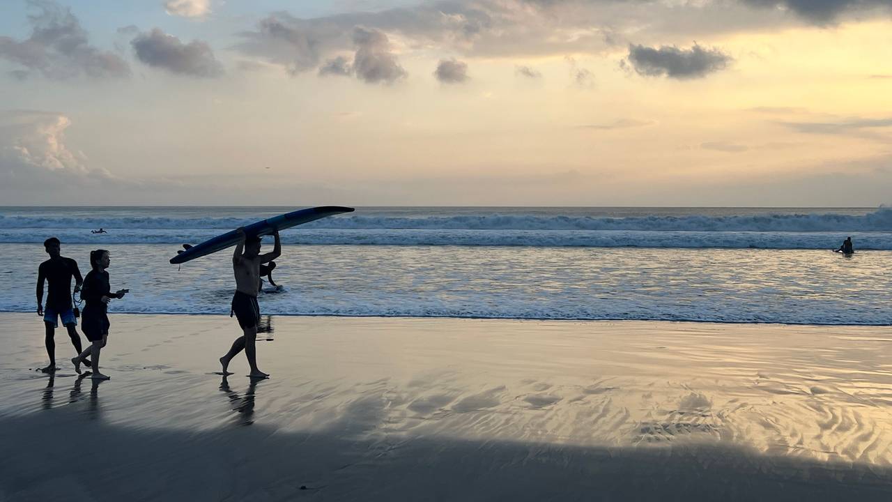 Ein Surfer läuft beim Sonnenuntergang mit seinem Surfbrett am Kuta Beach auf Bali.