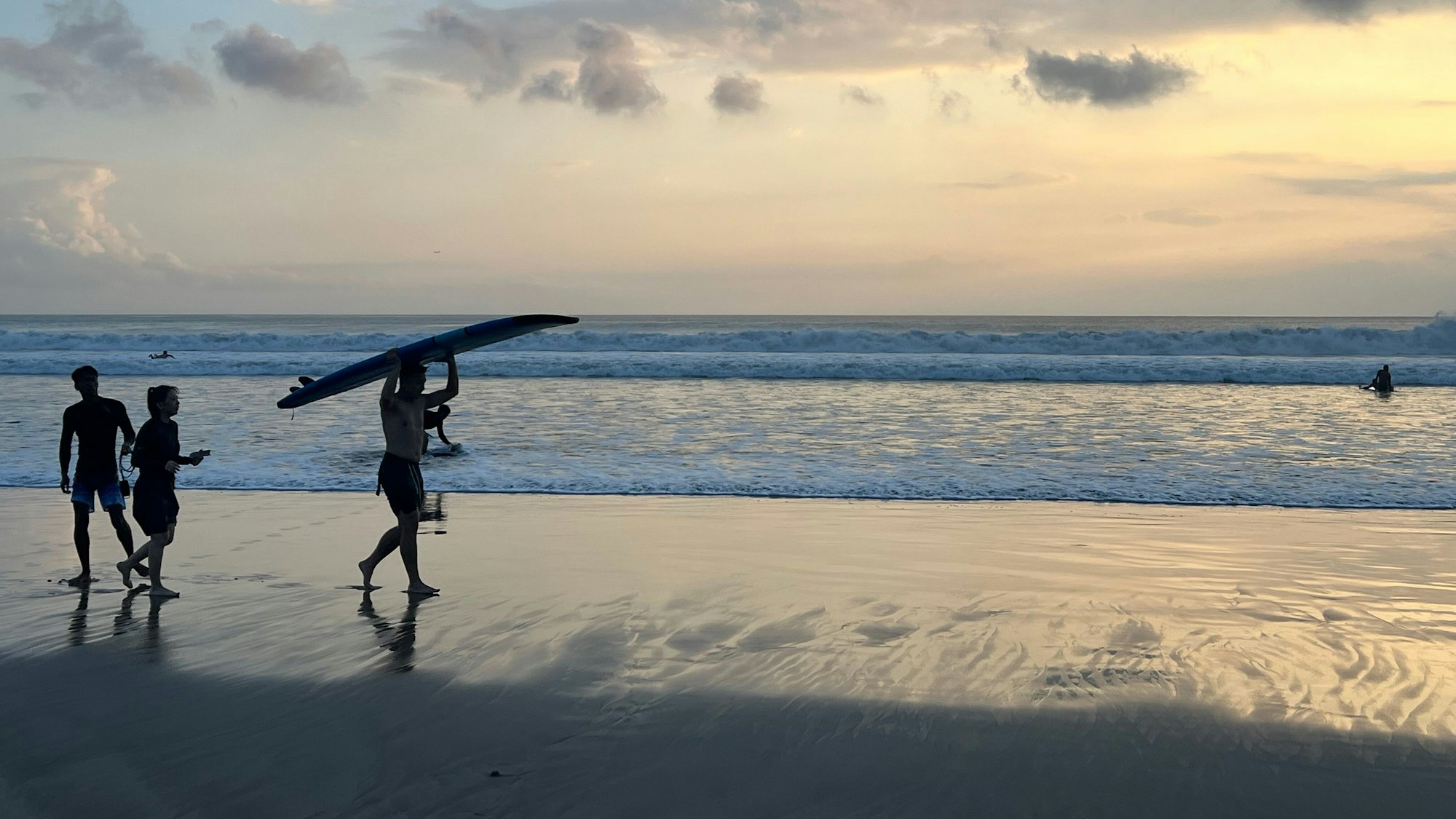 Ein Surfer läuft beim Sonnenuntergang mit seinem Surfbrett am Kuta Beach auf Bali.