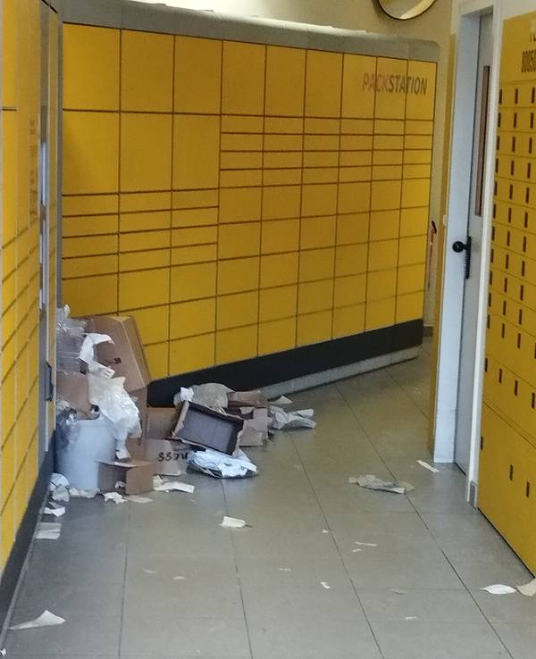 In einer Packstation liegen aufgerissene Pakete, Plastikverpackungen und Kartonfetzen auf dem Boden verstreut.