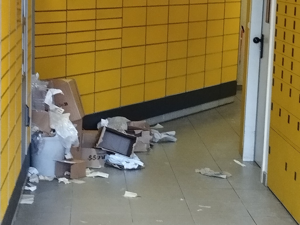 In einer Packstation liegen aufgerissene Pakete, Plastikverpackungen und Kartonfetzen auf dem Boden verstreut.