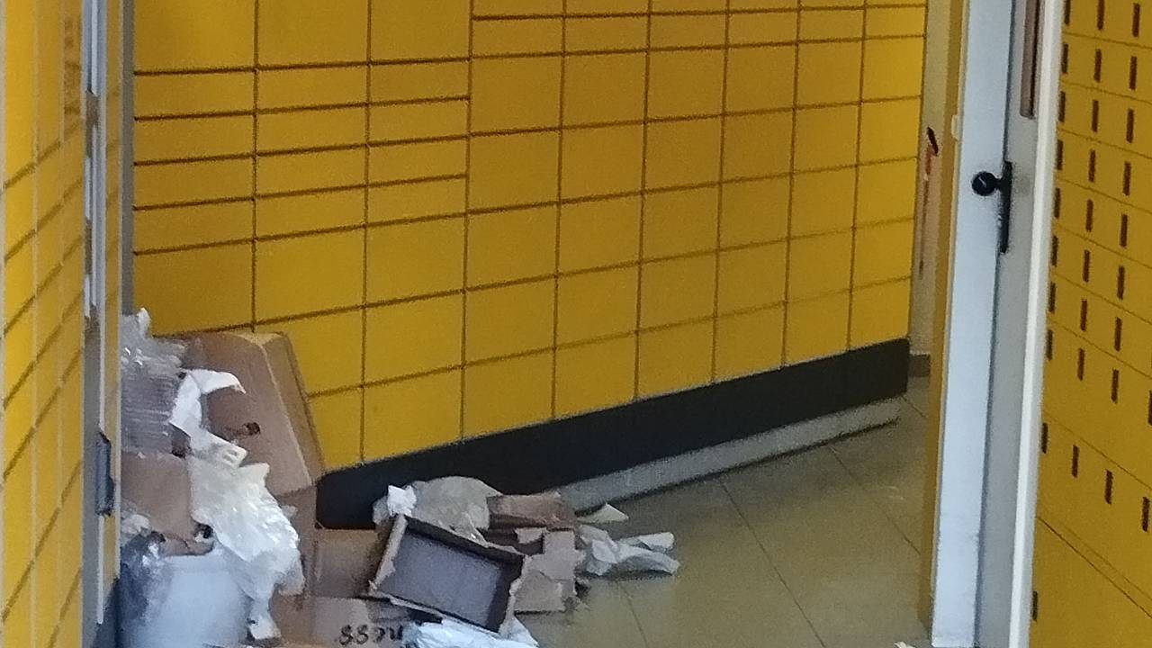 In einer Packstation liegen aufgerissene Pakete, Plastikverpackungen und Kartonfetzen auf dem Boden verstreut.