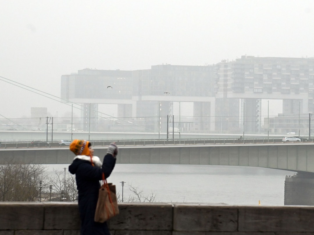 Eine Frau fotografiert am Rhein, im Hintergrund die Kranhäuser im Nebel.