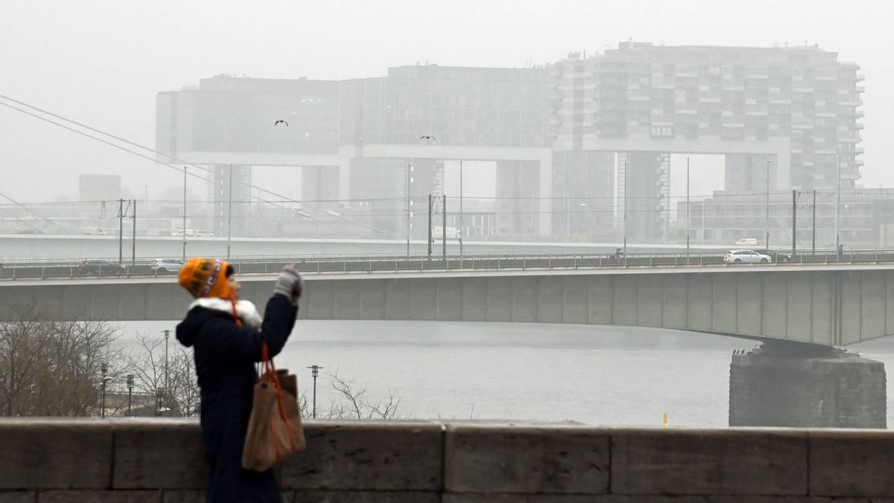 Eine Frau fotografiert am Rhein, im Hintergrund die Kranhäuser im Nebel.