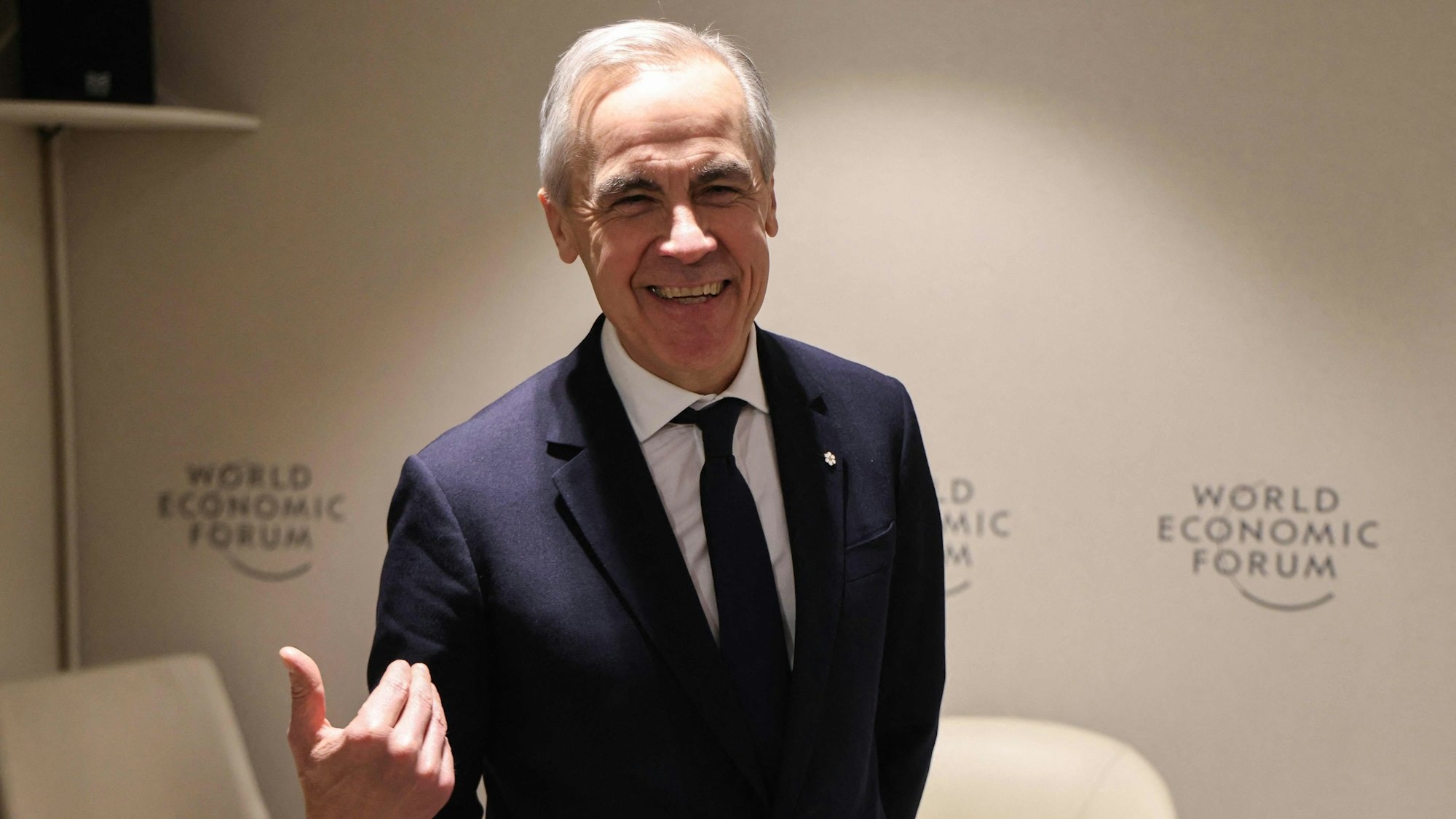 Ein Mann mit grauem Haar, in Anzug und mit Krawatte, gestikuliert und lacht dabei in die Kamera.