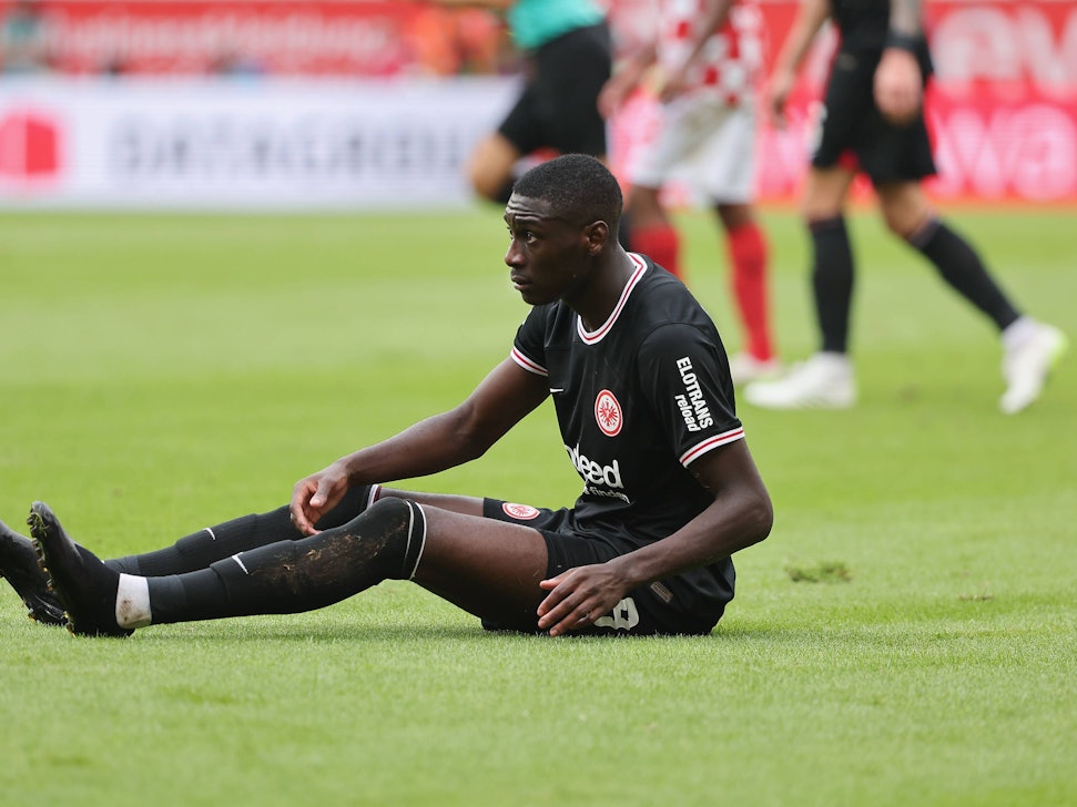 Randal Kolo Muani sitzt im Frankfurt-Trikot auf dem Rasen.