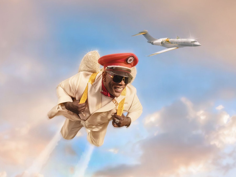 Ein fröhlich wirkender Mann in hellem Anzug und roter Mütze fliegt mit einem Düsenrucksack durch den Himmel. Hinter ihm zieht ein elegantes Privatflugzeug seine Bahn durch die pastellfarbenen Wolken.