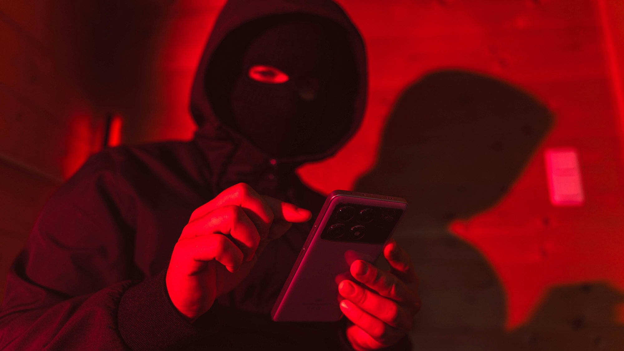 Anonymer Täter mit Maske benutzt Smartphone