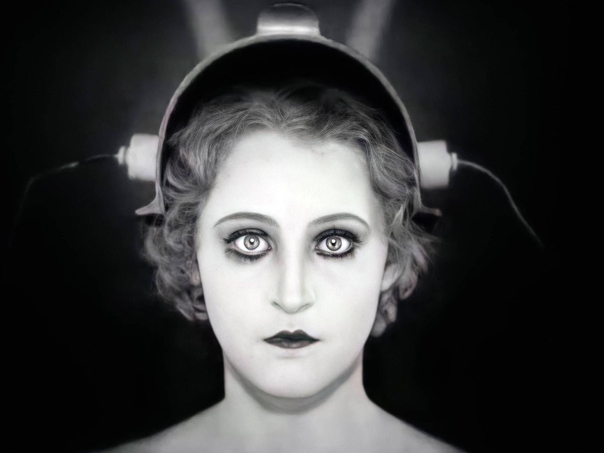 Eine Frau mit weitaufgerissenen Augen trägt einen Helm, an dem Stromanschlüsse zu sehen sind.