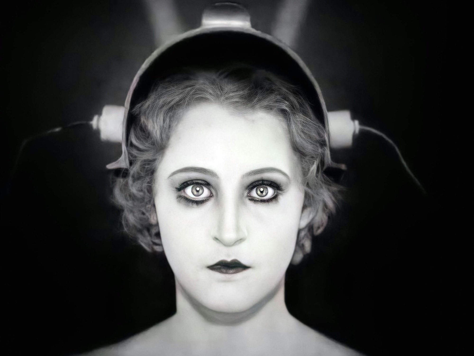 Eine Frau mit weitaufgerissenen Augen trägt einen Helm, an dem Stromanschlüsse zu sehen sind.