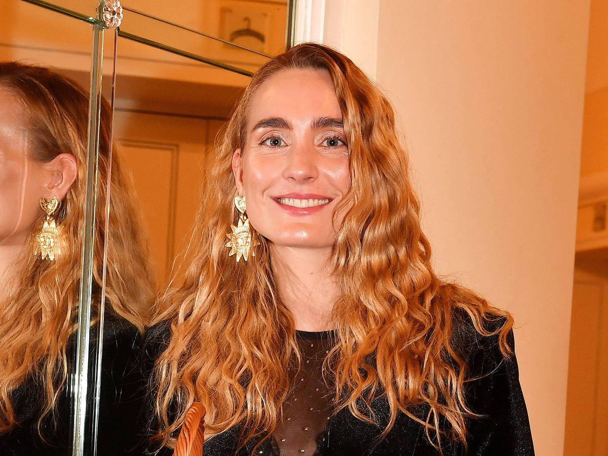 Verena Ofarim steht neben einem Spiegel und lächelt.