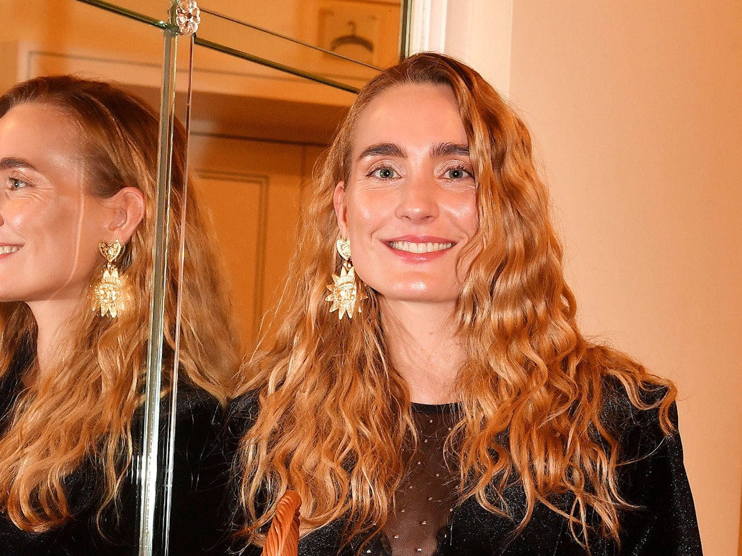 Verena Ofarim steht neben einem Spiegel und lächelt.