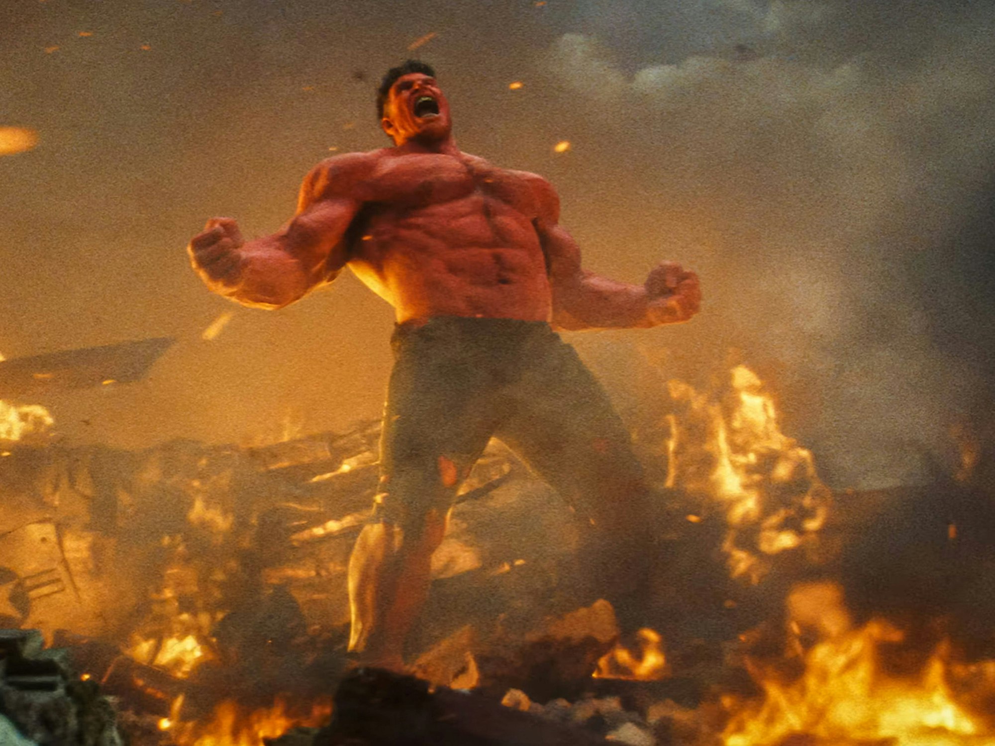 Ein übergroßer Mann mit mächtigen Muskeln und nacktem Oberkörper steht schreiend in einer dystopischen Umgebung mit Flammen und Rauch.