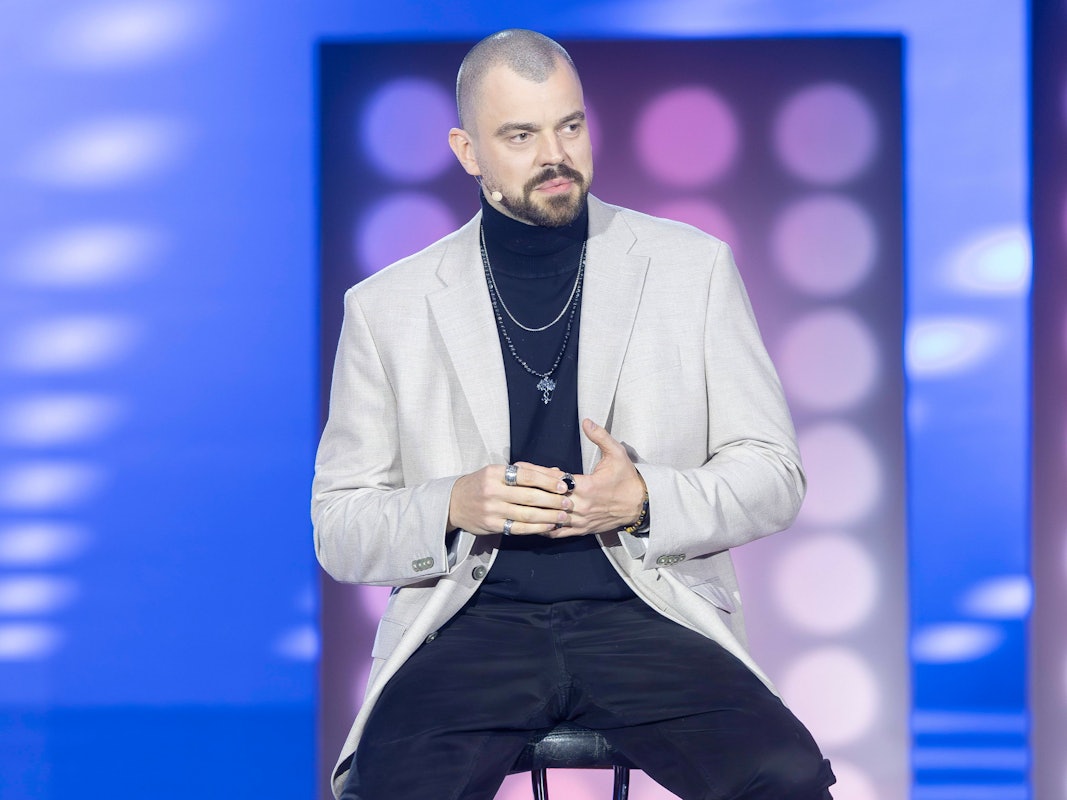 Ein Mann mit Glatze und Vollbart sitzt auf einem Barhocker und schaut aufmerksam.