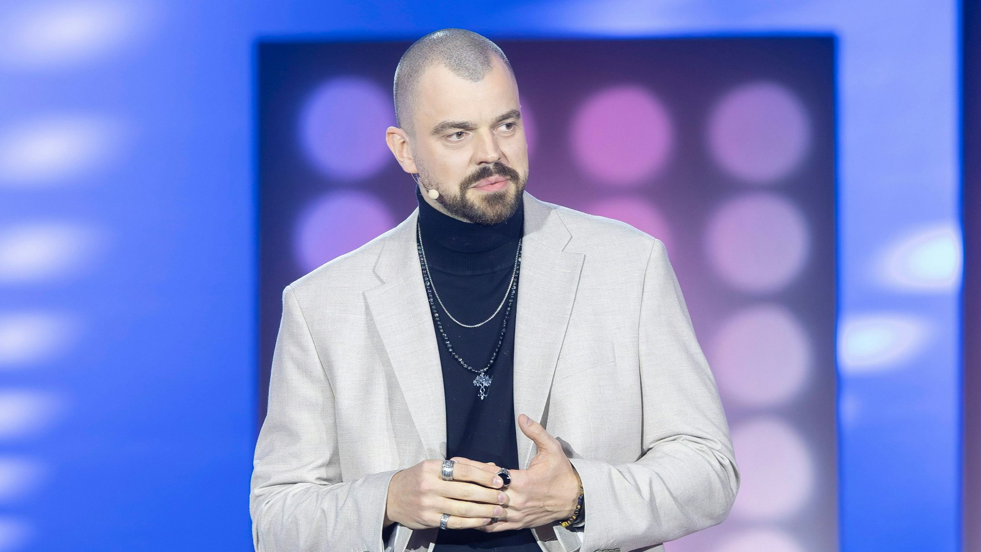 Ein Mann mit Glatze und Vollbart sitzt auf einem Barhocker und schaut aufmerksam.