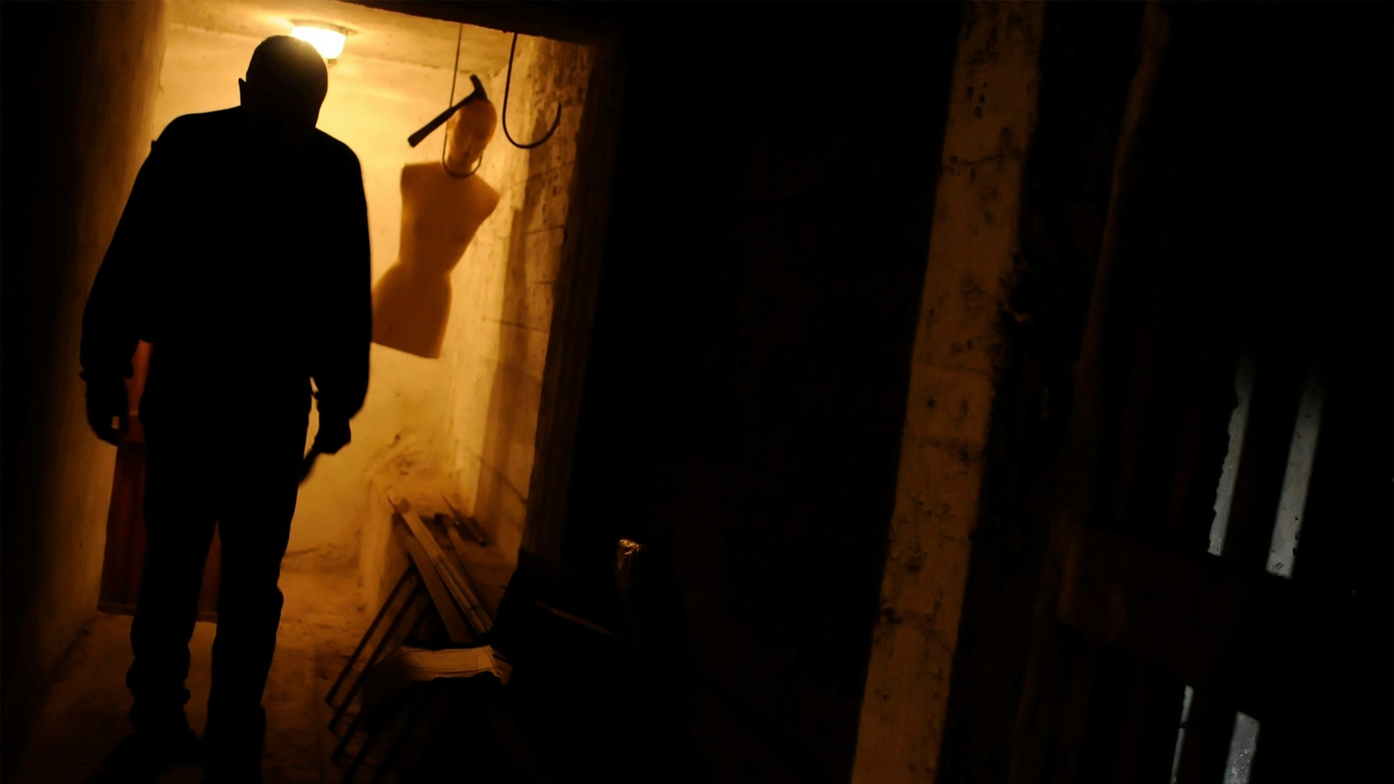 Schreckliche Szene – ein Verrückter in einem Keller mit einer hängenden Schaufensterpuppe.