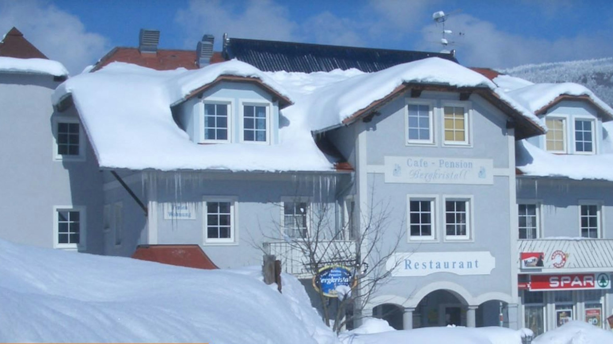 Ein hellblaues Hotelgebäude mit mehreren Erkern ist von einer dicken Schneedecke bedeckt.