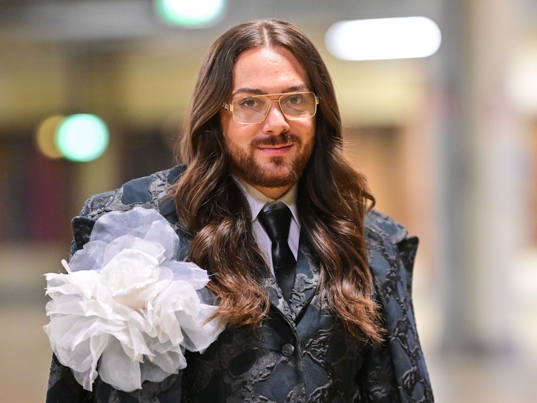 Riccardo Simonetti, Moderator und Autor, trägit einen Anzug mit Krawatte und einer großen Stoffblume.