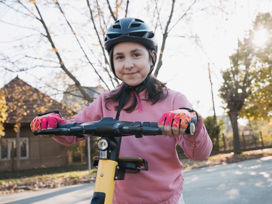 Kind auf Elektroroller mit Helm und Handschuhen