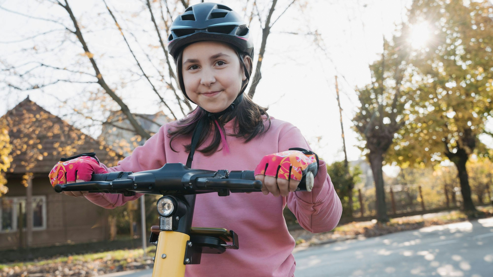 Kind auf Elektroroller mit Helm und Handschuhen