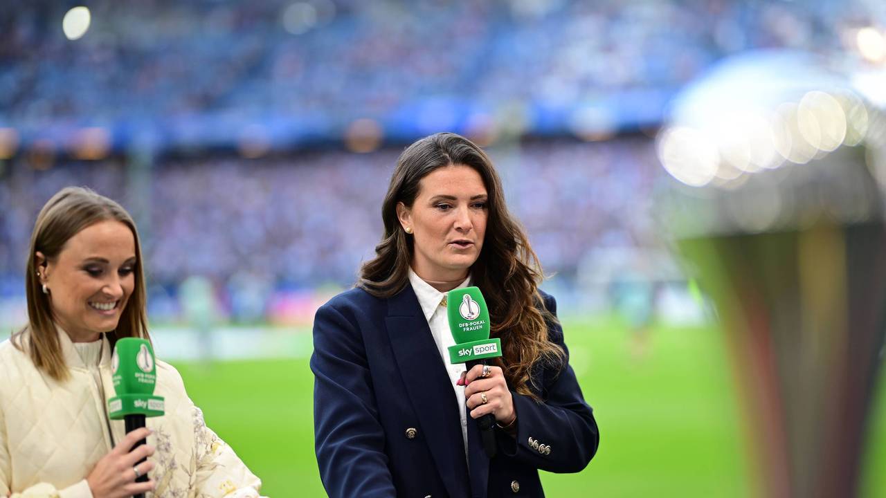 Rachel Rinast und Nele Ocik stehen mit Mikrofonen in der Hand am Spielfeldrand.