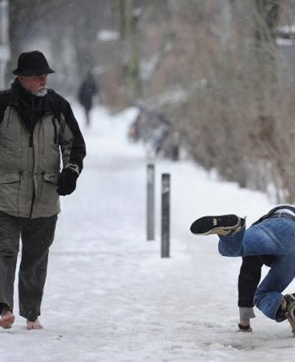 Ein Mann rutscht auf schneebedecktem Fußweg aus, ein anderer guckt hin.