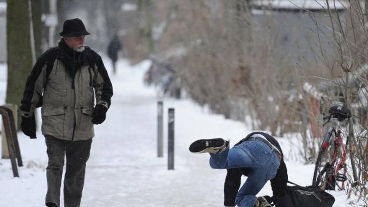Ein Mann rutscht auf schneebedecktem Fußweg aus, ein anderer guckt hin.