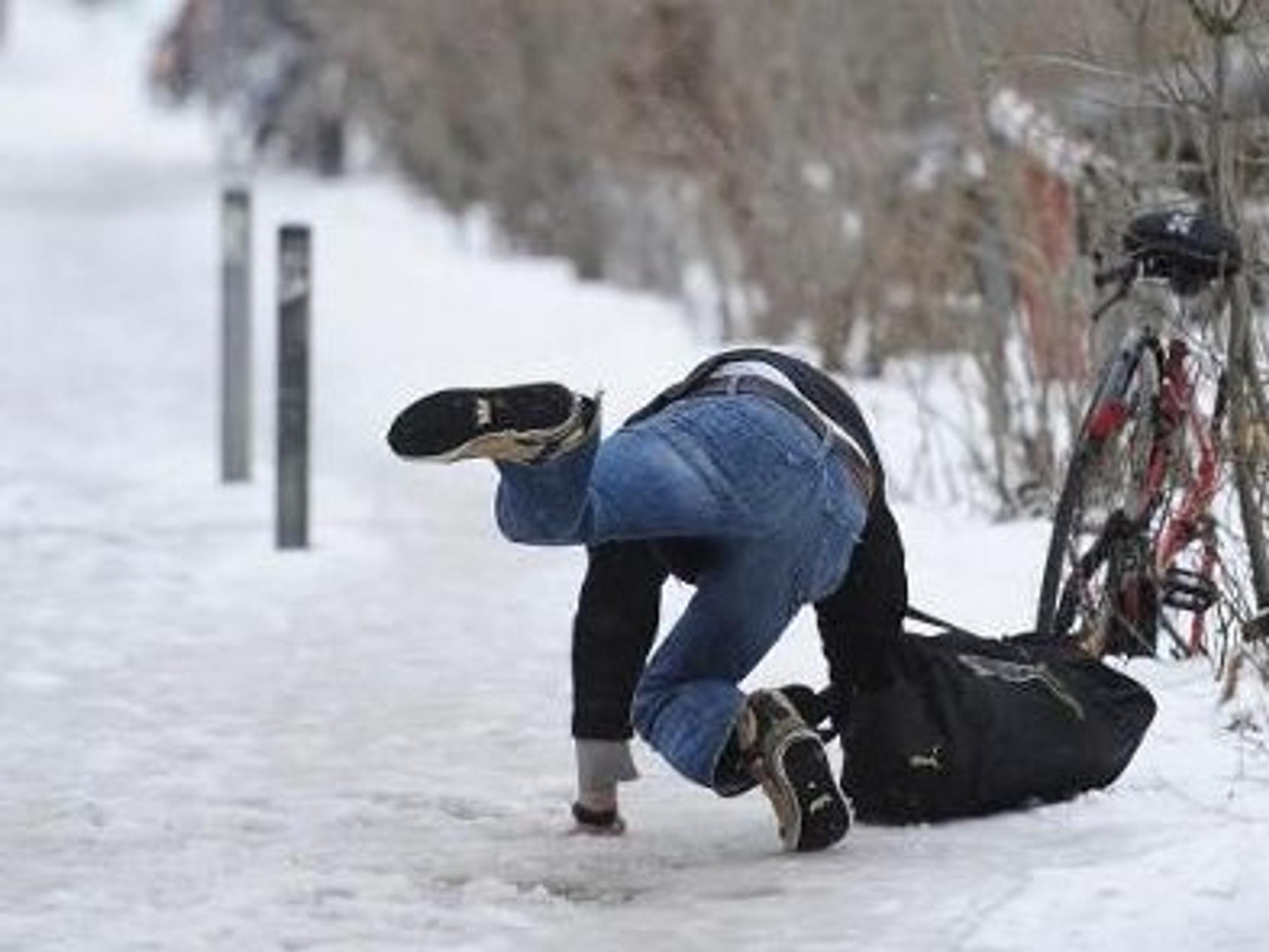 Ein Mann rutscht auf schneebedecktem Fußweg aus, ein anderer guckt hin.