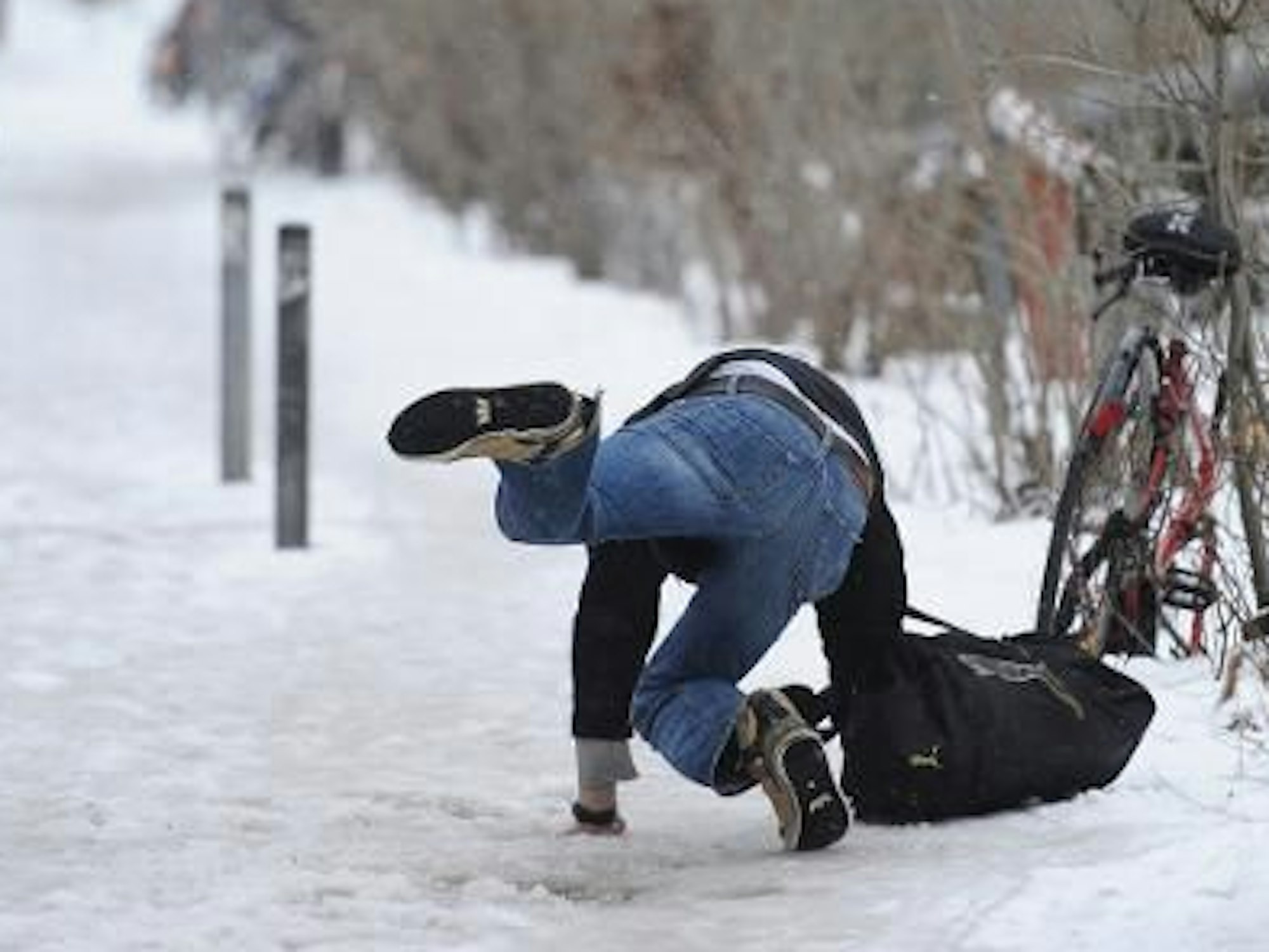 Ein Mann rutscht auf schneebedecktem Fußweg aus, ein anderer guckt hin.