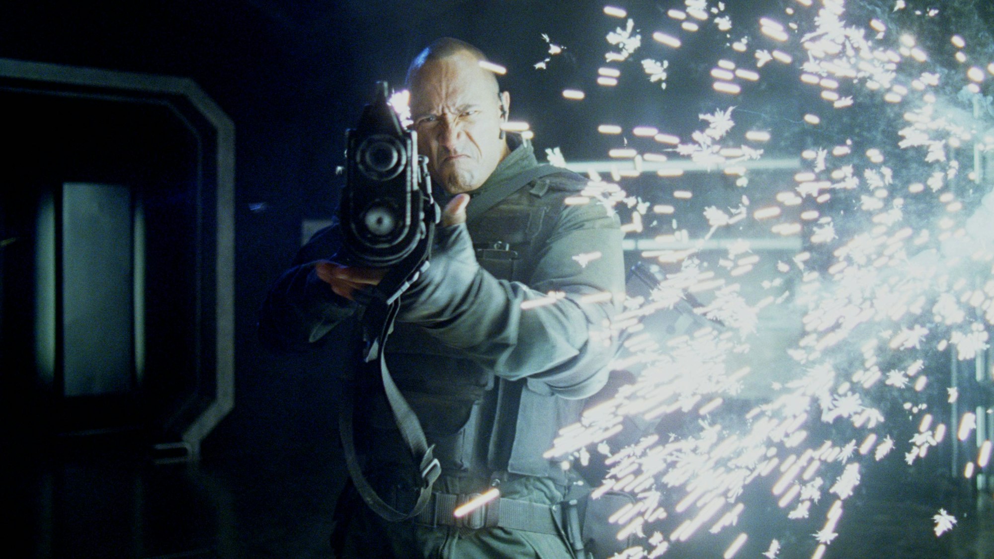 Ein Mann mit einer flakähnlichen Waffe schießt, während im Hintergrund Funken stieben.