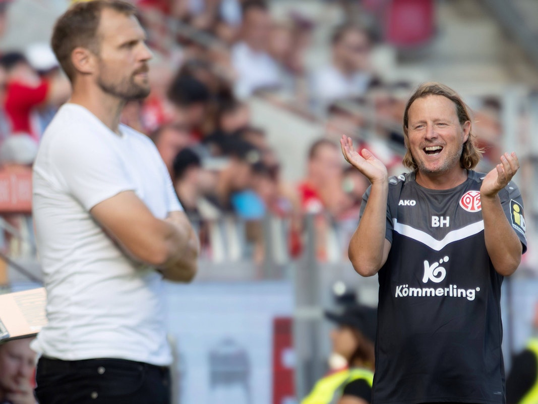 Bo Henriksen lacht, im Vordergrund ist unscharf Bo Svensson zu sehen, der die Arme verschränkt hat.