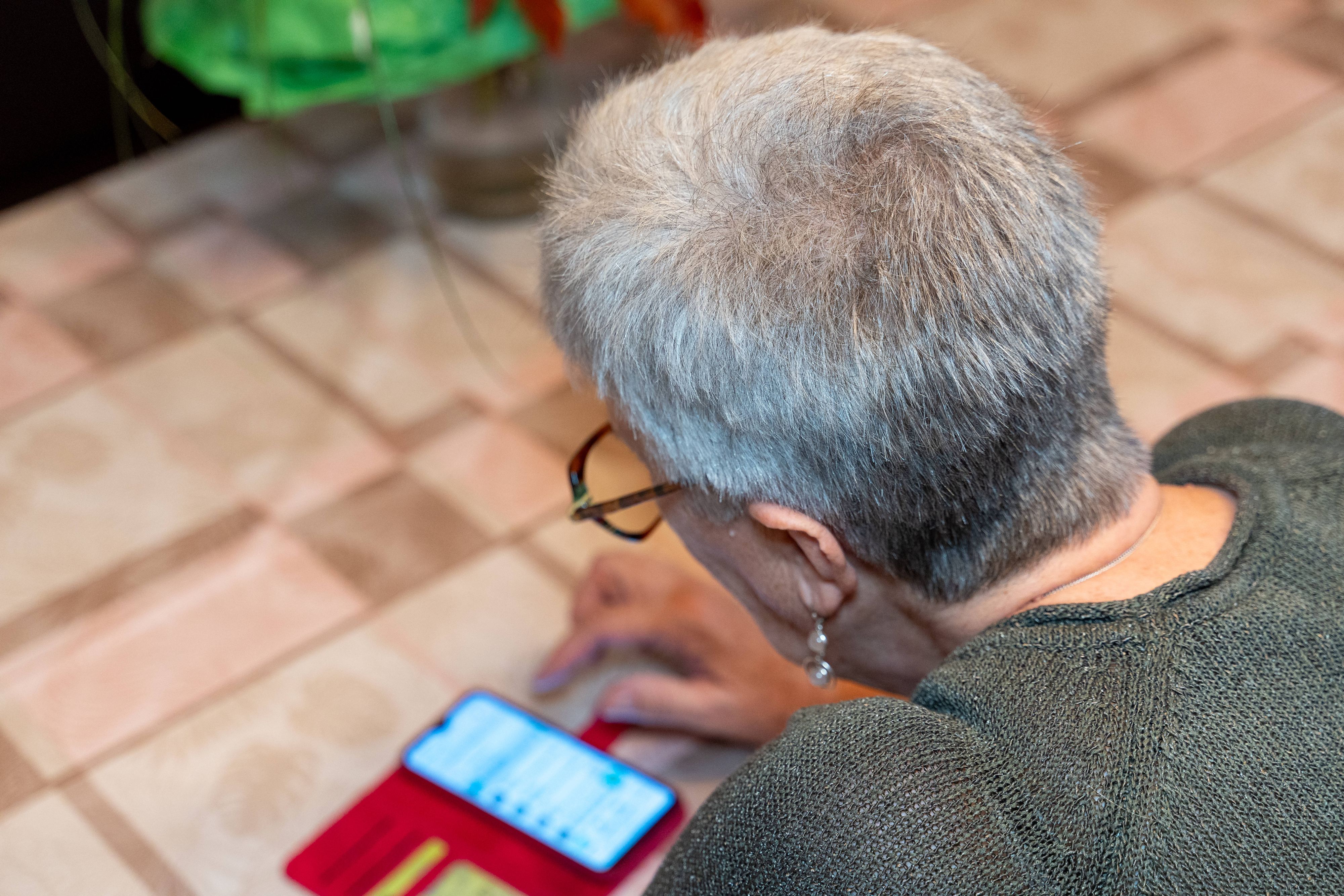 Ältere Frau tippt auf Smartphone am Tisch