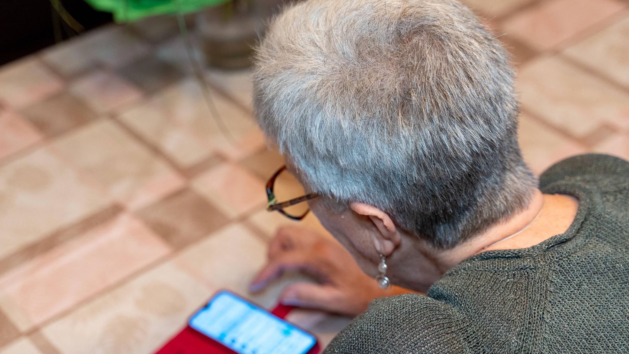 Ältere Frau tippt auf Smartphone am Tisch