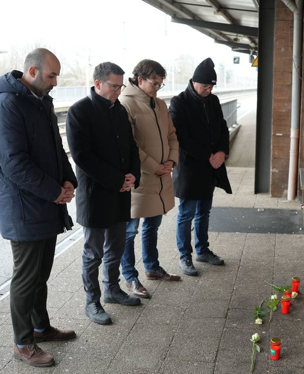 Menschen stehen vor Blumen und Kerzen am Bahnsteig im Gedenken an den Tod eines Zugbegleiters. Der Mann war bei einem Angriff im Zug von einem Fahrgast am Montagabend in Rheinland-Pfalz lebensgefährlich verletzt worden und am Morgen infolge der Verletzungen verstorben.