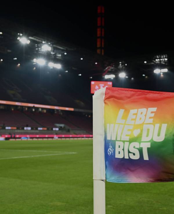 Eine Eckfahne im Rhein-Energie-Stadion in den Farben der Regenbogenflagge und der Aufschrift „Lebe wie du bist“.