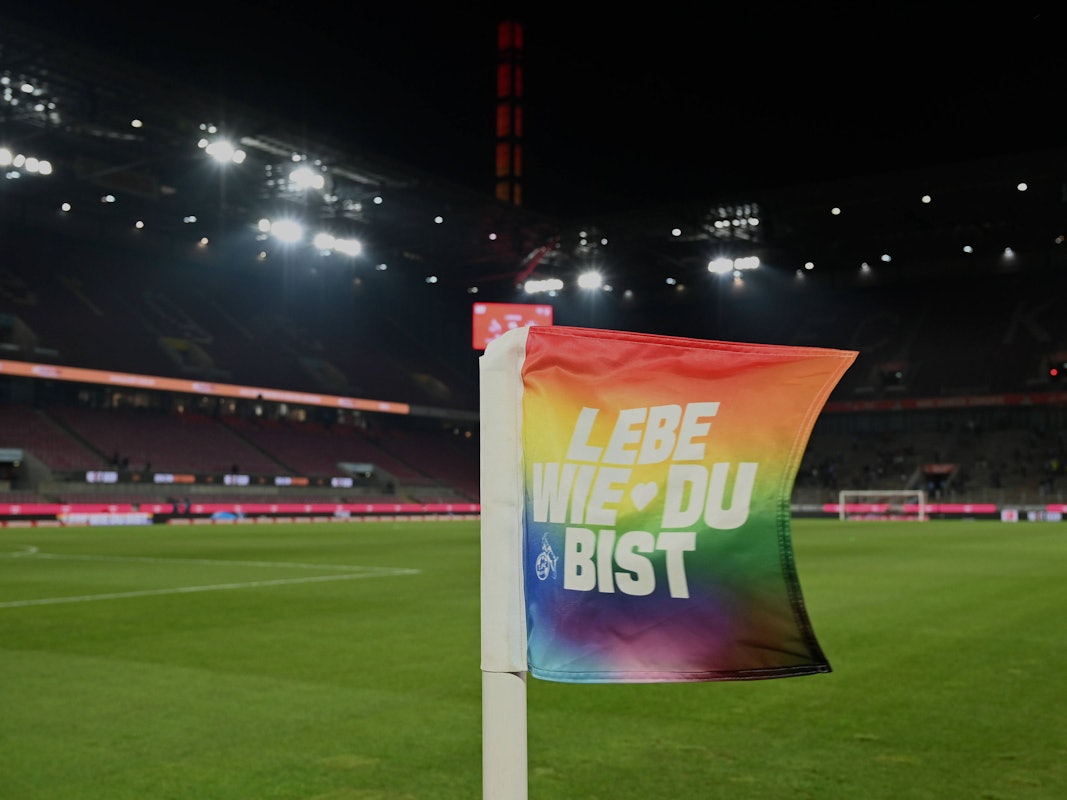 Eine Eckfahne im Rhein-Energie-Stadion in den Farben der Regenbogenflagge und der Aufschrift „Lebe wie du bist“.