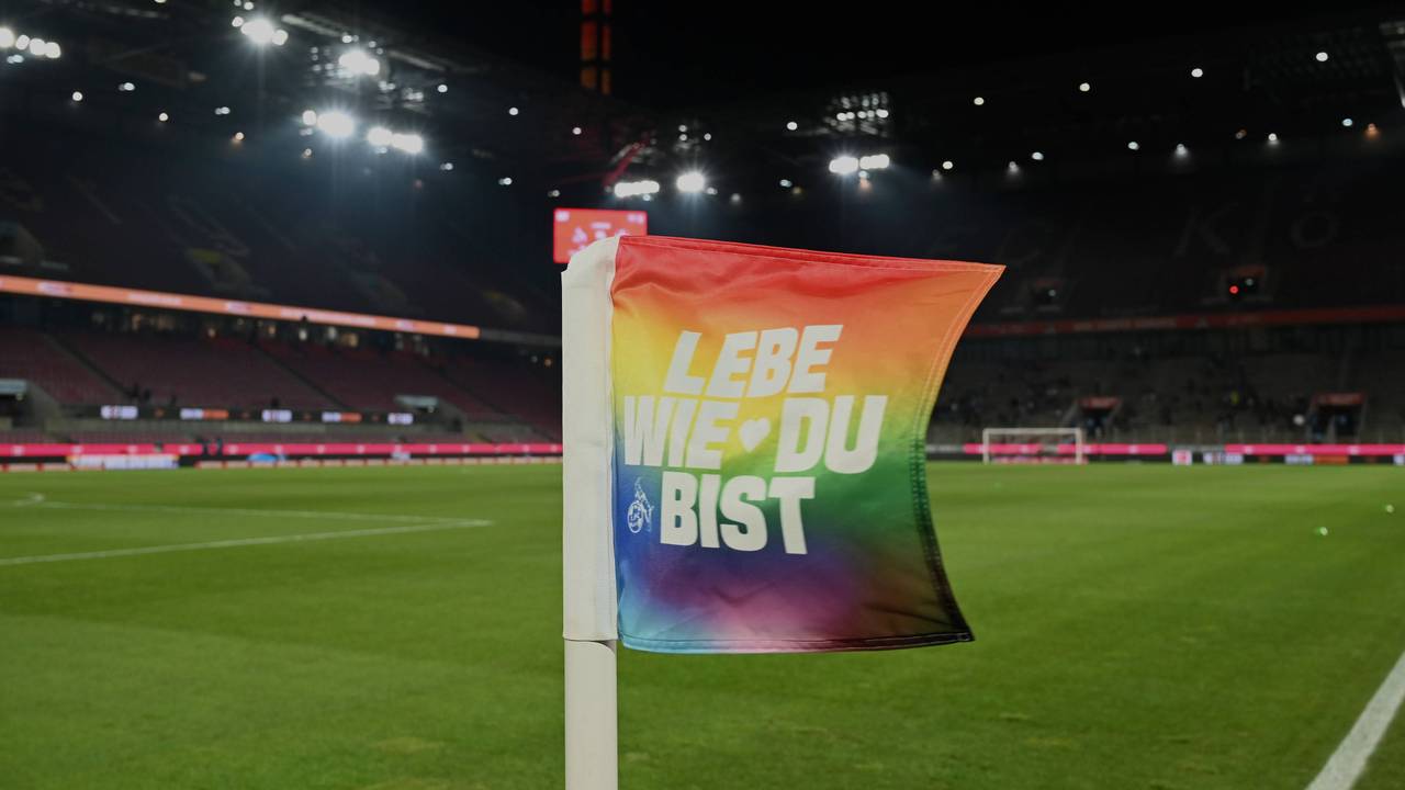 Eine Eckfahne im Rhein-Energie-Stadion in den Farben der Regenbogenflagge und der Aufschrift „Lebe wie du bist“.