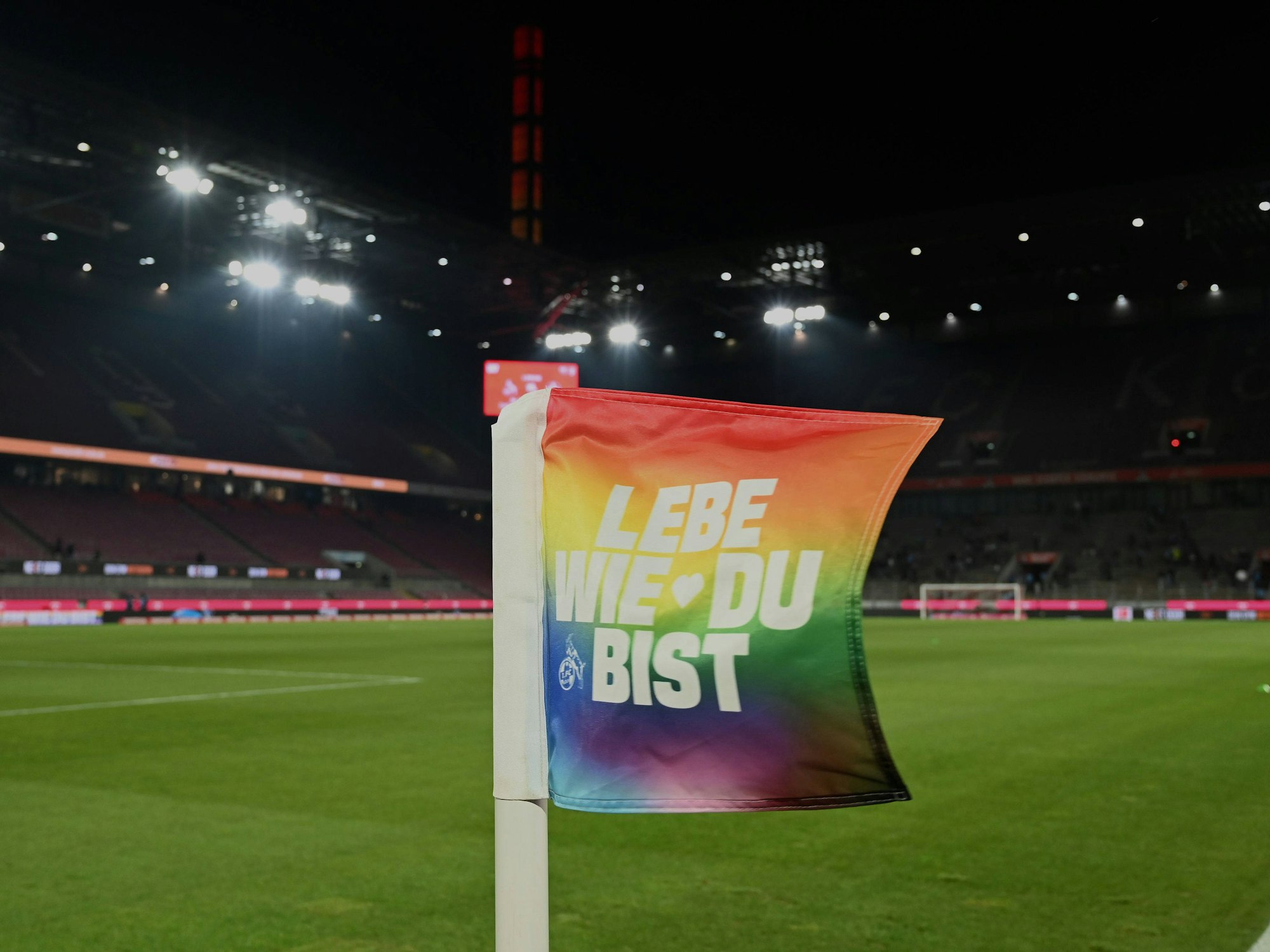 Eine Eckfahne im Rhein-Energie-Stadion in den Farben der Regenbogenflagge und der Aufschrift „Lebe wie du bist“.