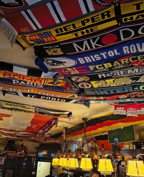 Fußballschals und Fahnen hängen in einer Kneipe an der Decke.