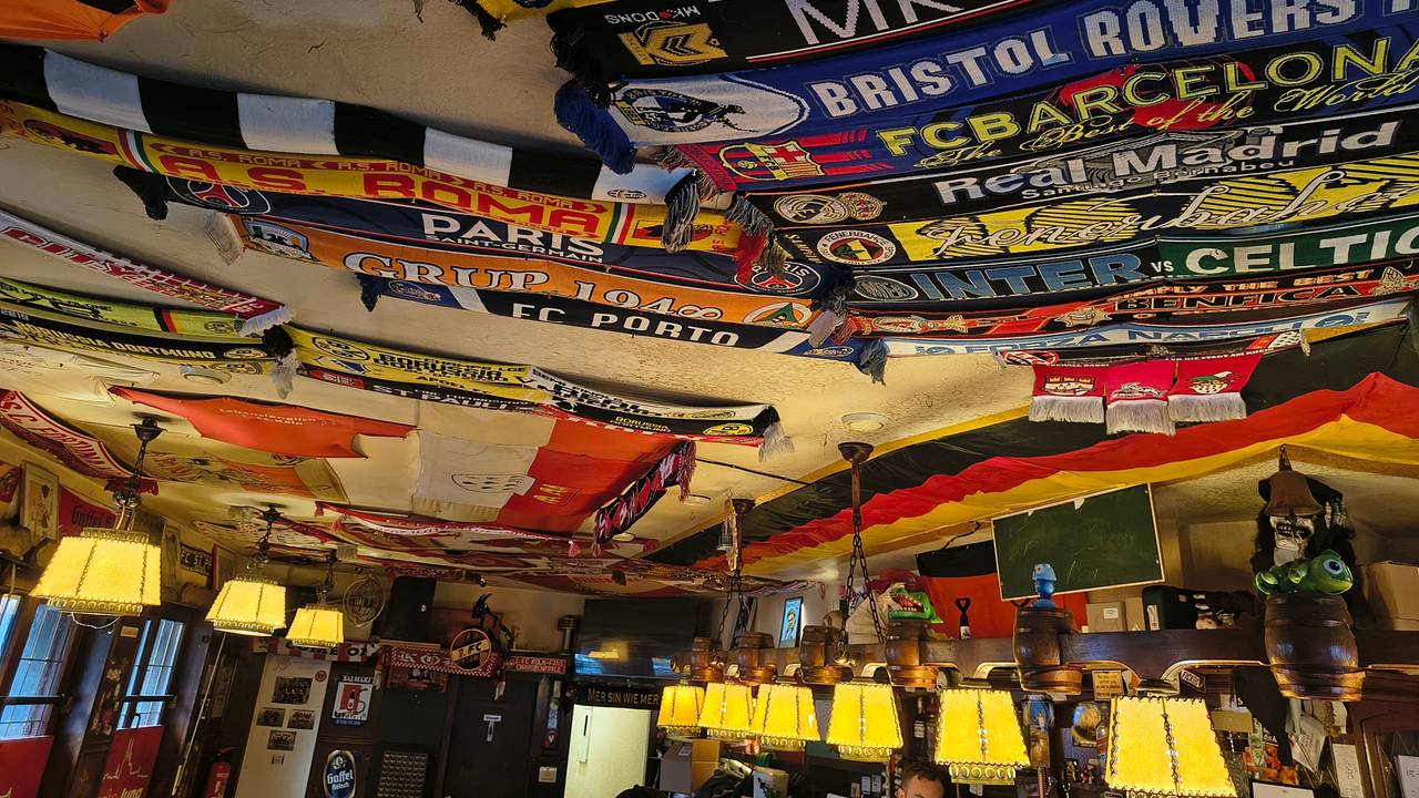 Fußballschals und Fahnen hängen in einer Kneipe an der Decke.