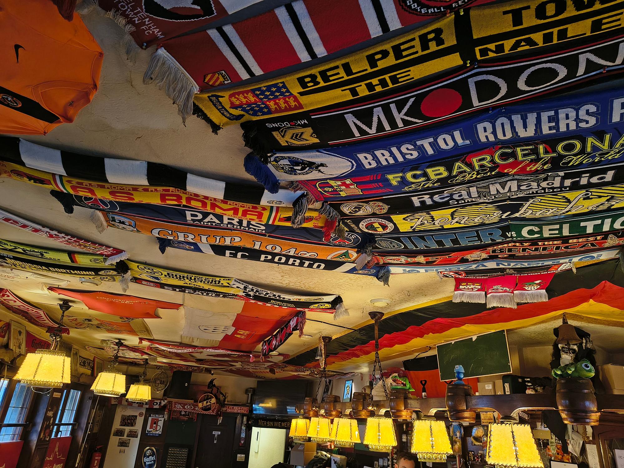 Fußballschals und Fahnen hängen in einer Kneipe an der Decke.