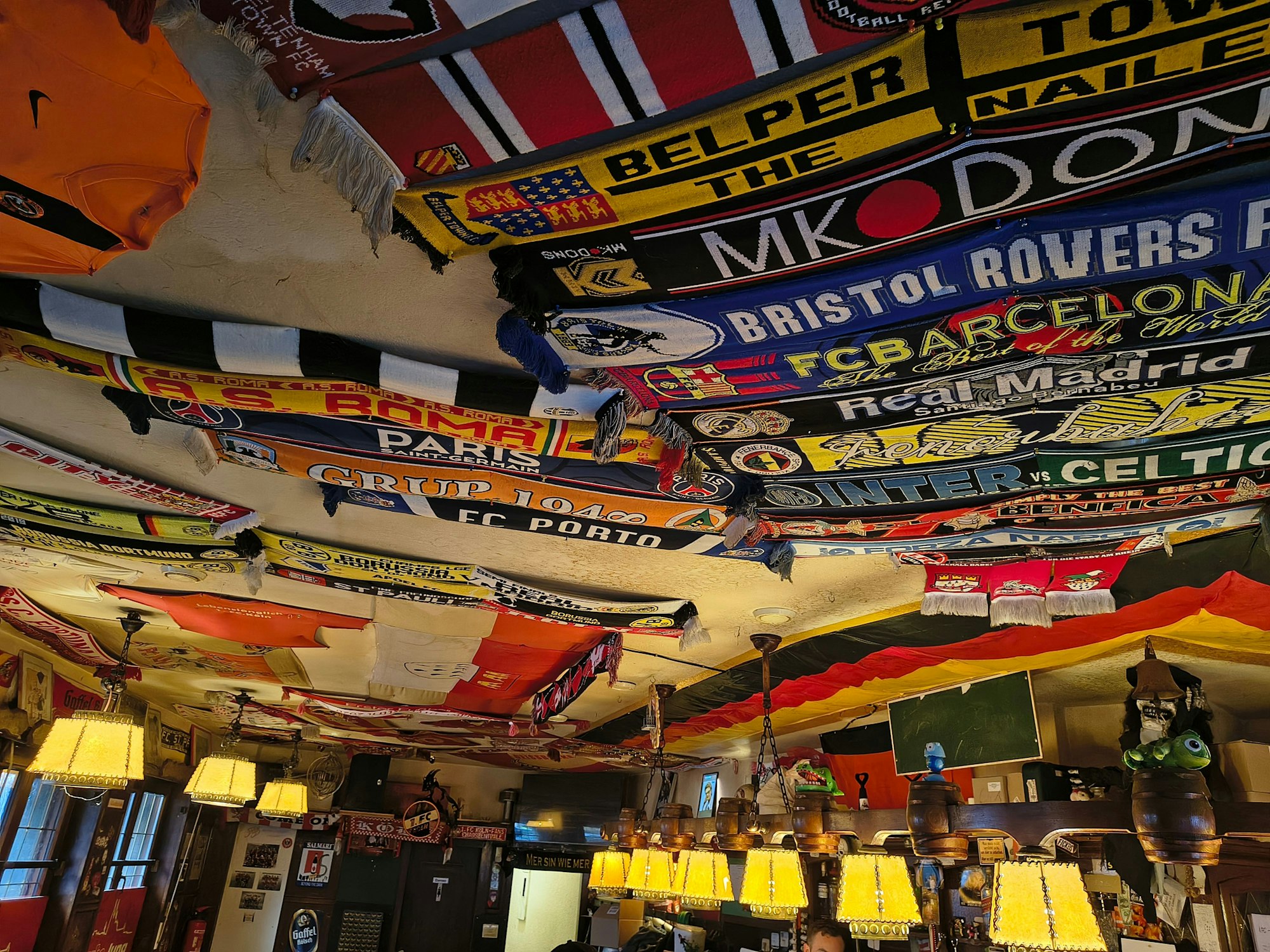 Fußballschals und Fahnen hängen in einer Kneipe an der Decke.