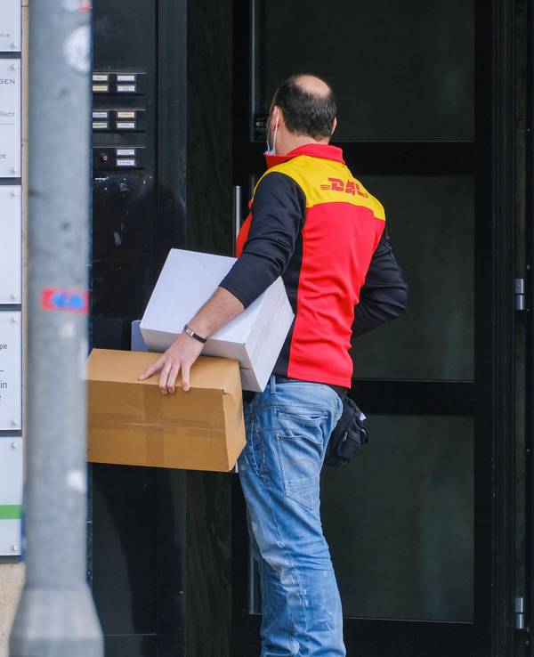Ein Paketbote von DHL steht vor einer verschlossenen Tür.