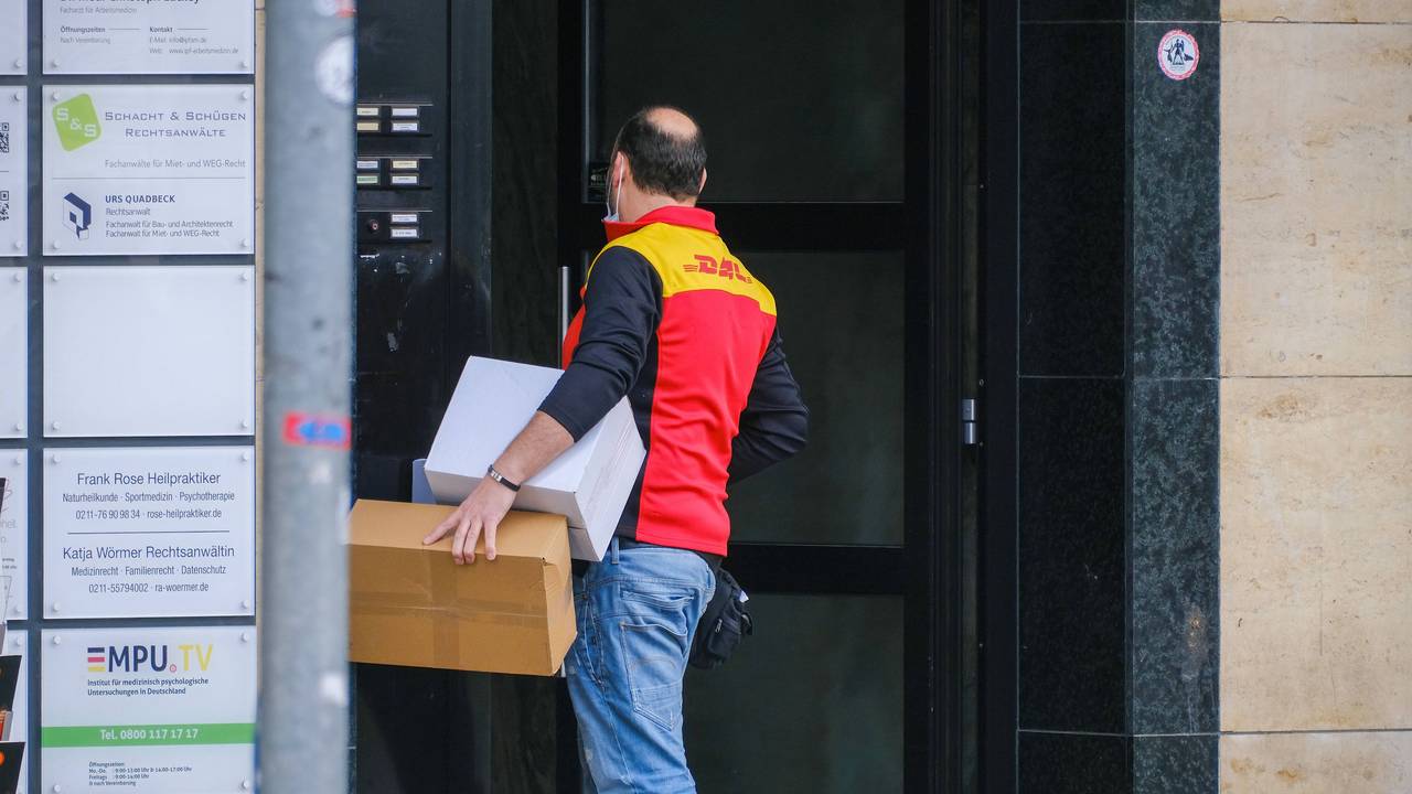 Ein Paketbote von DHL steht vor einer verschlossenen Tür.