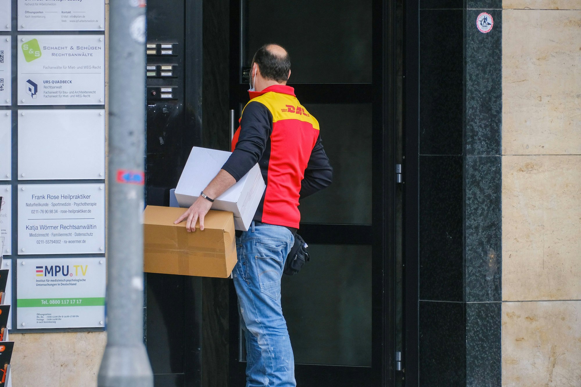 Ein Paketbote von DHL steht vor einer verschlossenen Tür.